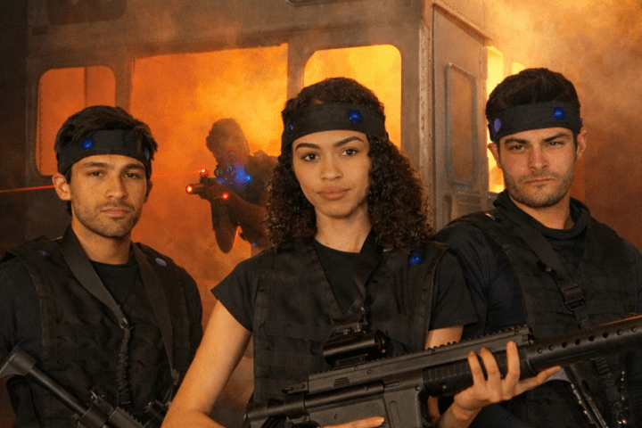 Three people in tactical gear with toy guns stand in front of a smoky background.