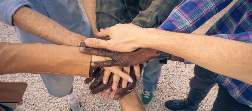 Nine hands of diverse people stacked in a gesture of unity.