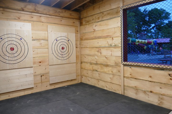 Indoor axe throwing range with two wooden targets and window showing outdoor scene.