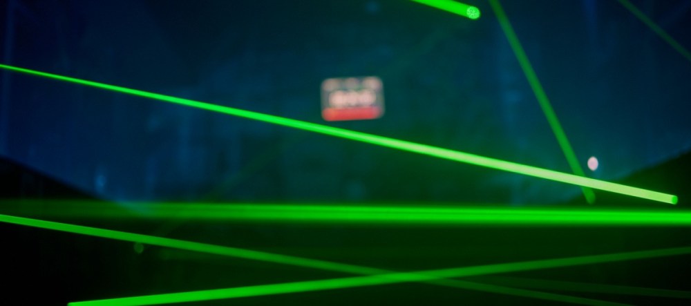 Green laser beams crisscross in a dark room with a red exit sign.