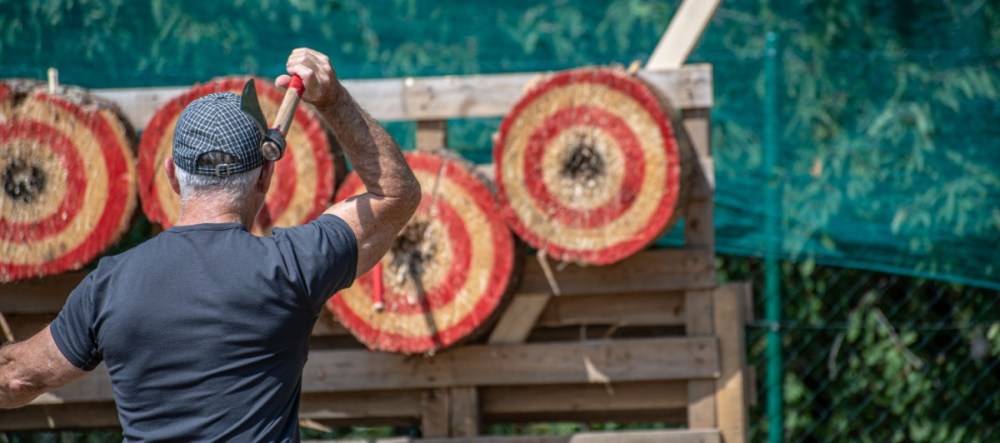 Man throwing an axe at circular red and yellow targets outdoors.