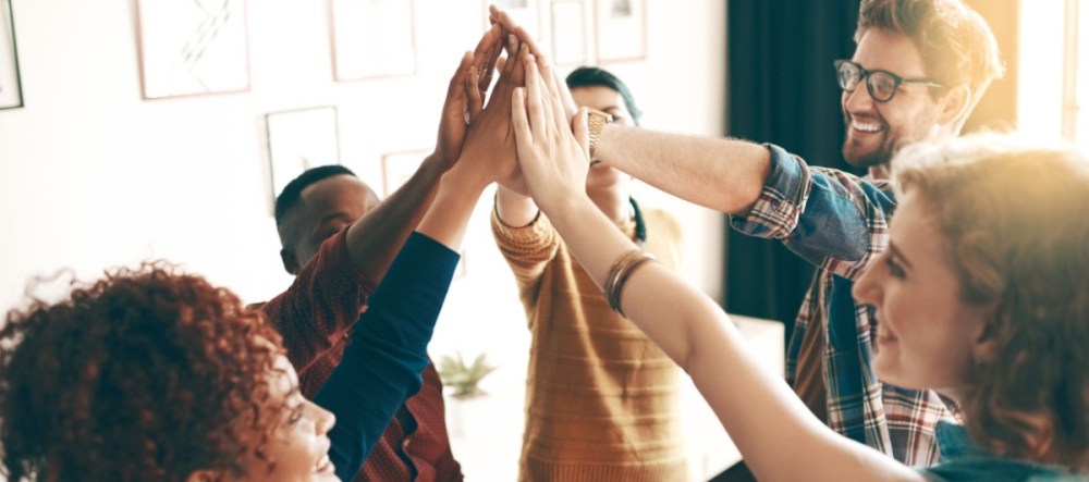 Group of diverse people joining hands in a high-five, showing teamwork and unity, indoors.