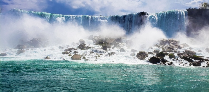 Majestic waterfall with mist and rocky foreground under a blue sky.