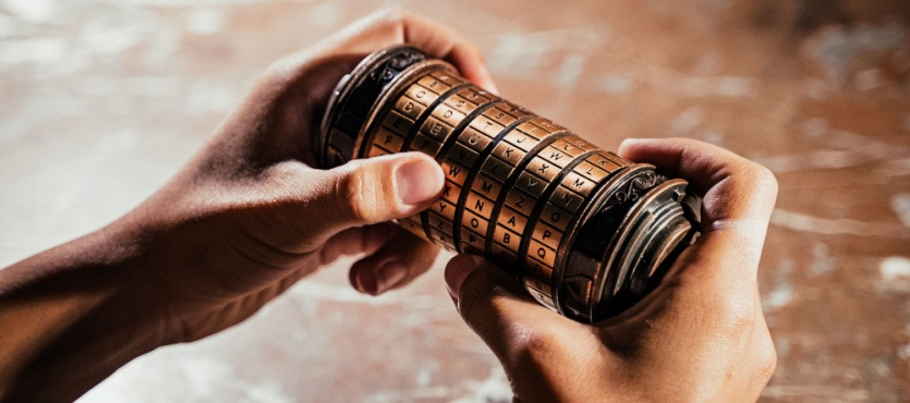 Hands holding a brass cryptex with rotating letter dials.