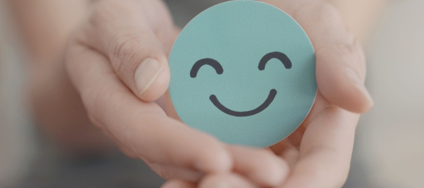 Hands holding a smiling face sticker on a blue circle.