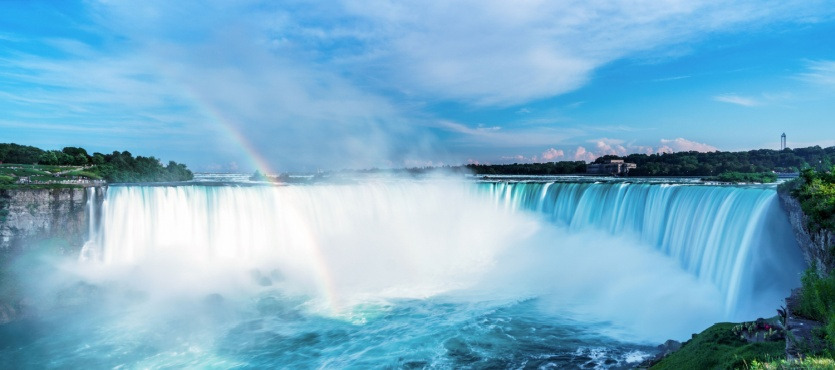 Panoramic view of a large waterfall with a rainbow under a blue sky.