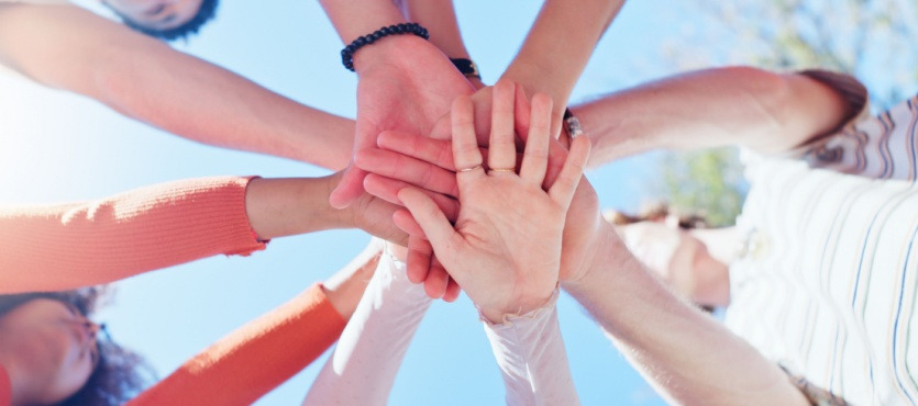 Diverse group of hands joined together against a blue sky.