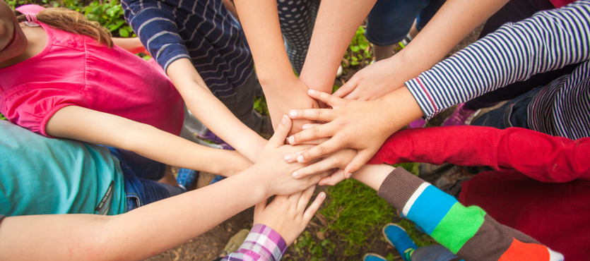 Group of children putting their hands together in a circle outdoors.